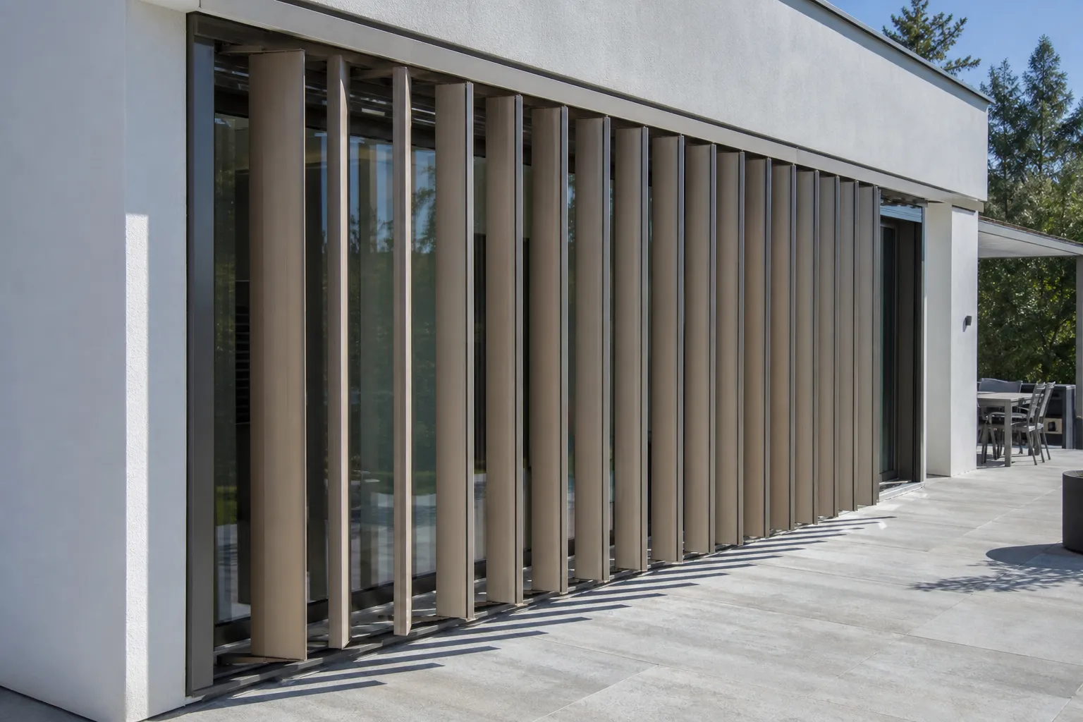 Brise-soleil orientable aluminium devant une grande baie vitrée, lames en position mi-ouverte