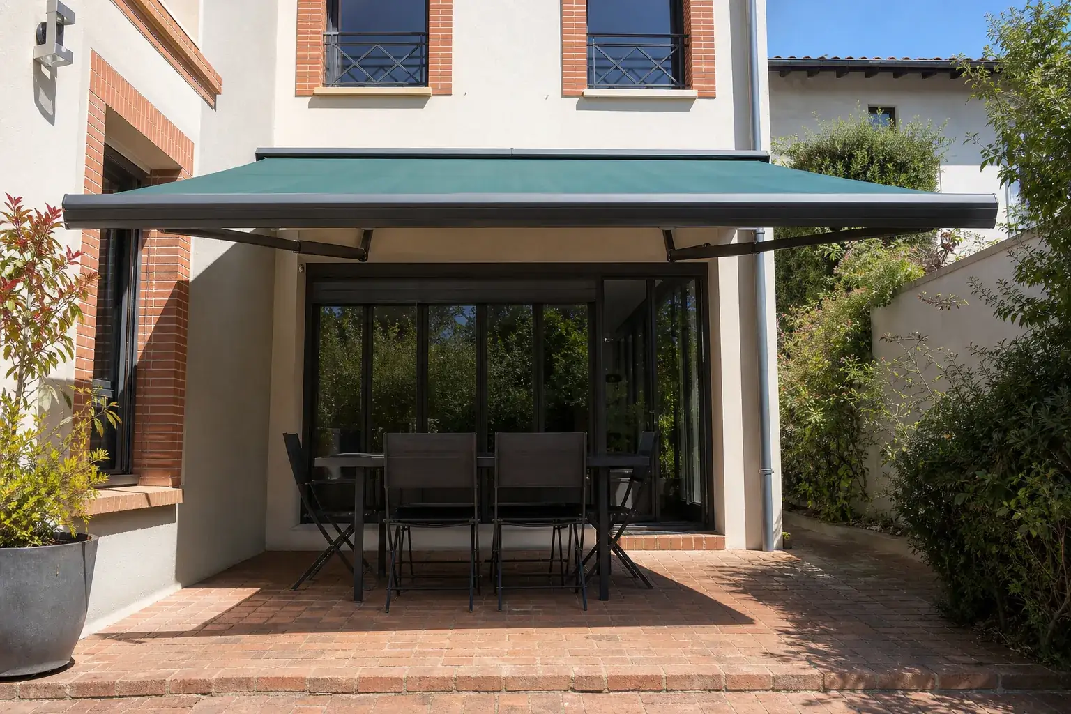Store banne à armature aluminium et toile bleu-vert déployé au-dessus d’une terrasse en brique
