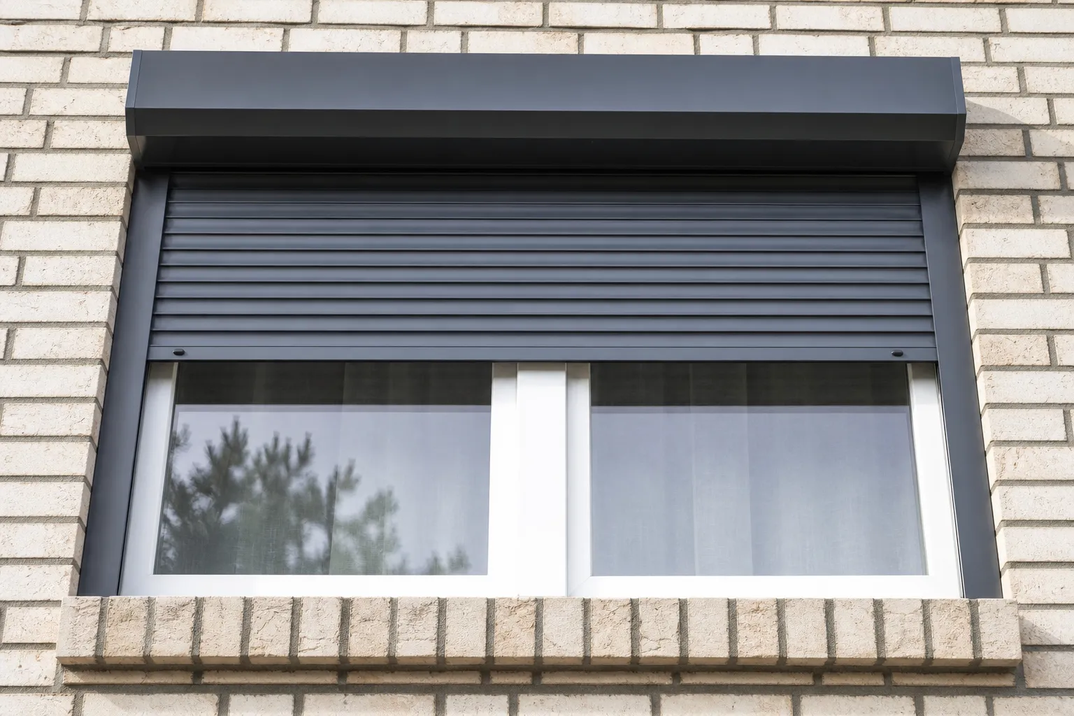 Coffre de volet roulant aluminium en applique sur une façade en brique claire, tablier à demi descendu