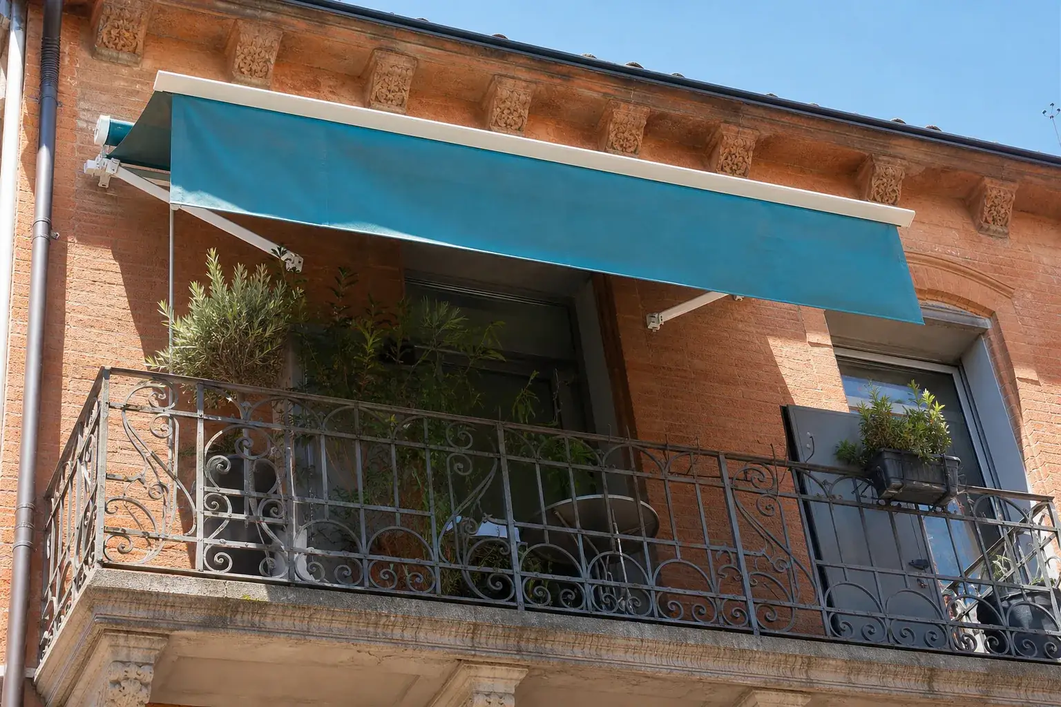 Store banne aluminium et toile bleu-vert déployé au-dessus d’un balcon d’immeuble toulousain en brique
